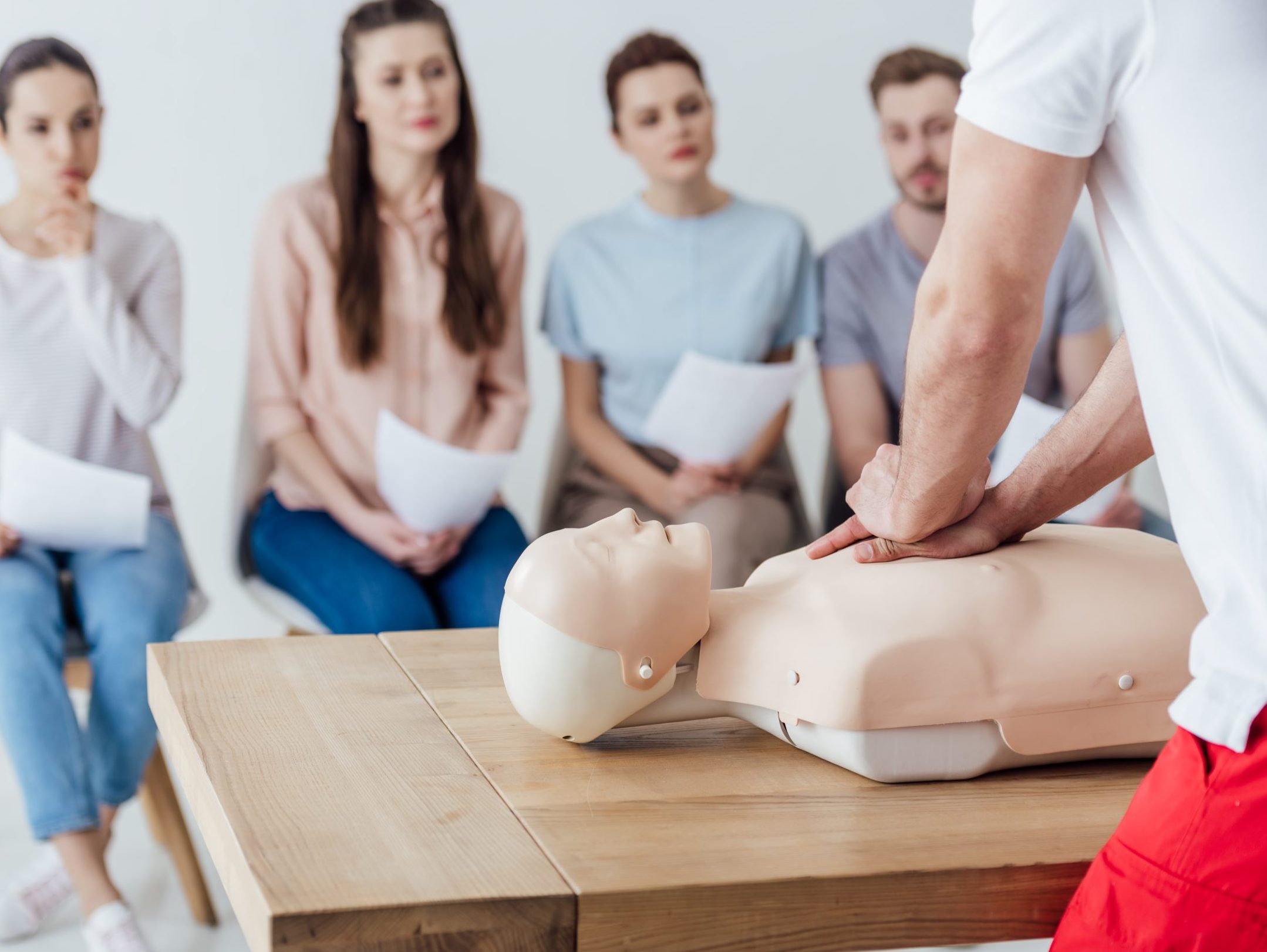 back view of instructor performing cpr on dummy during first aid training with group of people